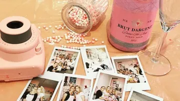 Eine pinke Kamera umgeben von Fotos und Sektflasche.