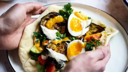One hand holds a flatbread filled with vegetables.