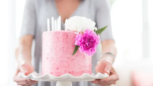 A person is holding a pink cake with flowers.