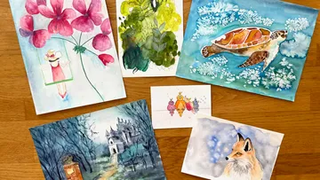 Watercolor paintings lie on a wooden table.