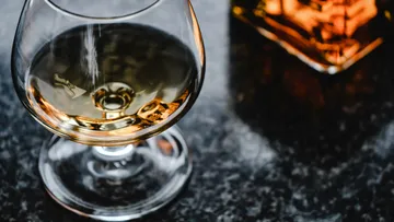 A glass of golden drink is on a dark table.