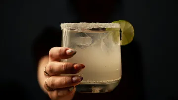 Hand holding cocktail glass with salt rim and lime slice.