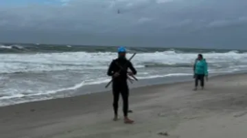 A surfer with equipment is walking along the beach.