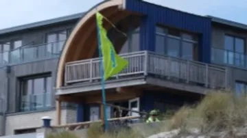 Bright building with balcony and green flag on the beach.
