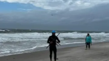 Person mit Ausrüstung geht am stürmischen Strand entlang.
