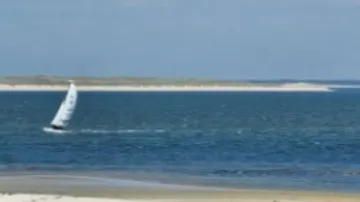 Segelboot fährt über das Wasser, umgeben von Küste.
