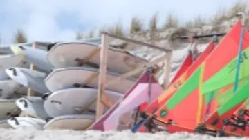 Surfboards and windsurfing boards are available on the beach.