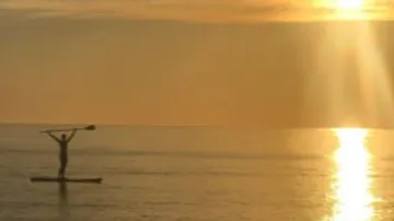 Person paddelt auf einem Board bei Sonnenuntergang im Wasser.