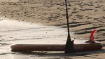 Stehpaddelbrett im Sand mit Paddel daneben am Wasser.