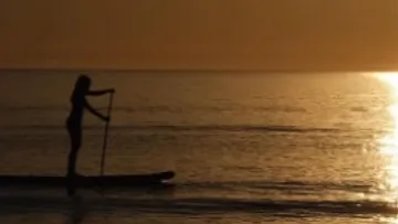 Stehpaddelnde Person auf ruhigem Wasser bei Sonnenuntergang.