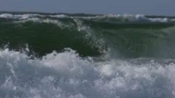 Welle bricht, umgeben von schäumendem Wasser und Himmel.