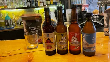 There are four beer bottles on a wooden counter, next to a glass.