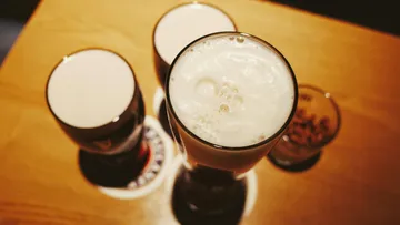There are three glasses of beer on a table.