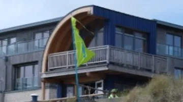 Bunte Fahne weht vor modernem Gebäude am Strand.