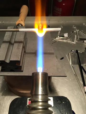 A burner heats a glass rod in a workshop.