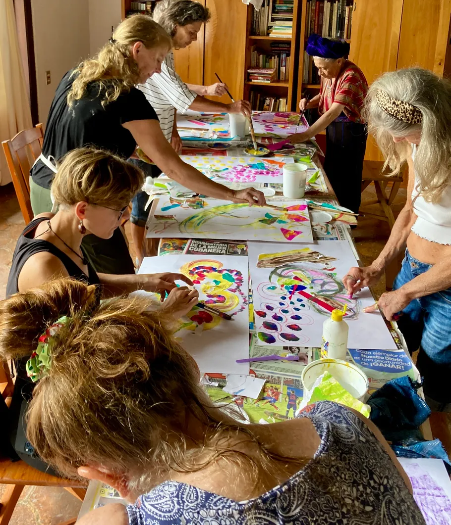 Six women paint colorfully at a table.