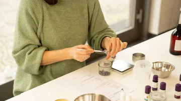 Eine Person mischt Zutaten in einem Glasbehälter am Tisch.