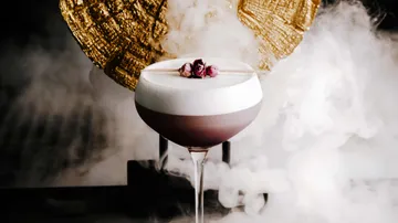 A cocktail is sitting on a table surrounded by smoke.