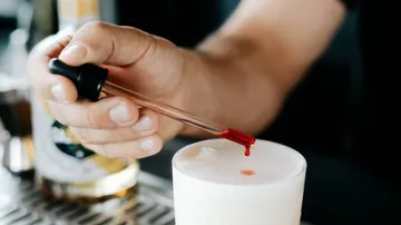 A hand drops red content into a drink.