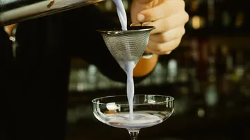Ein Cocktail wird durch ein Sieb in ein Glas gegossen.