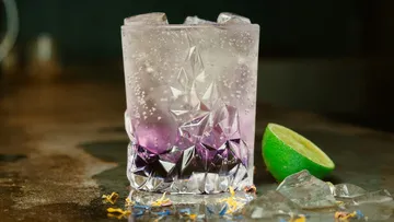 Ein Glas mit Eis und lila Getränk steht auf einem Tisch.