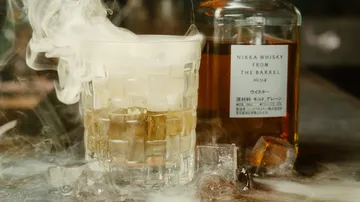 Glas mit Whisky raucht, neben einer Whiskyflasche.