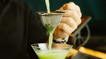 Green drink is poured through a sieve into a glass.