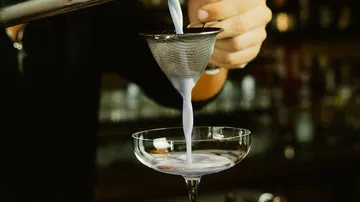 A bartender filters purple liquid into a glass.