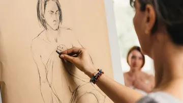 An artist draws a nude on paper in a studio.