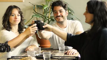 Four people toast with cups in a café.