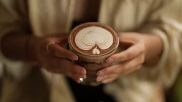 Glass with decorated coffee in hands, relaxing environment.