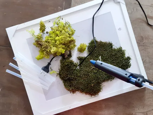 Moss is lying on a table while hot glue is being used.