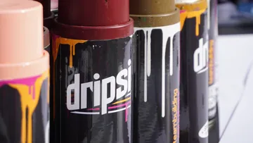 Paint cans are standing, paint is running down, art supplies are visible.