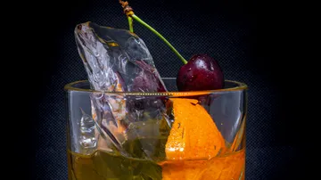 Ein Glas mit Eis, fruchtigen Zutaten und dunklem Hintergrund.