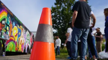 Pylon steht, während Menschen beim Graffiti malen versammelt sind.