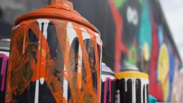 Spraydose mit orangefarbener Farbe vor bunter Wand.