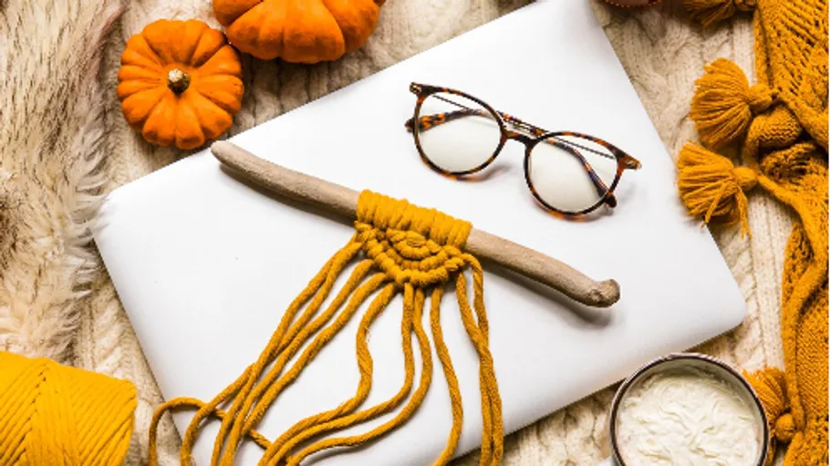 Garn und Brille liegen auf einem weißen Tisch mit Kürbissen.