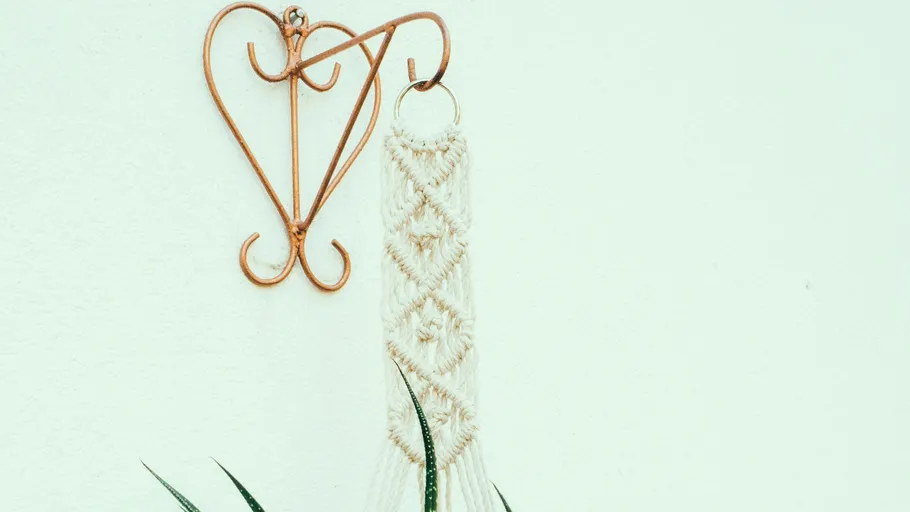 Ein Herzaufhänger hält einen Makramee-Pflanzenhalter an der Wand.