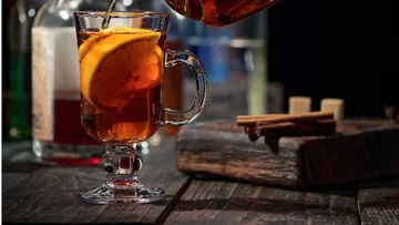 Ein Glas Tee wird aus einer Kanne gegossen. Holzoberfläche.
