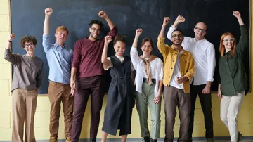 Group of people raise their arms, smile in front of blackboard.