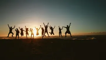 Several people jump on the beach before sunset.