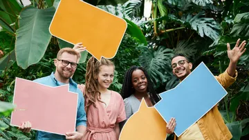 Four people hold colorful speech bubbles in a garden.