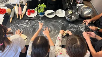 Children roll dough on a worktop dusted with flour.