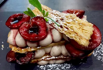 Layered dessert with cherries and cream, on a dark plate.