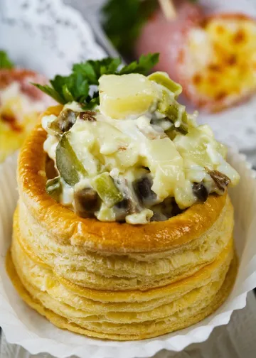 Blätterteigschale mit Salatfüllung, eingerahmt von weiteren Snacks.
