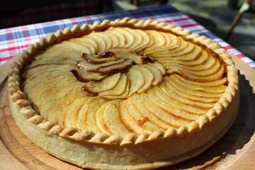 Apple pie on wooden board, outdoors in sunlight.
