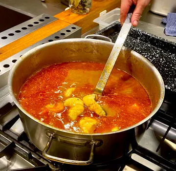 Ein Topf mit kochender Suppe wird umgerührt.