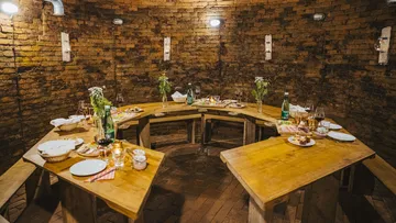 Round wooden tables with laid food in a brick room.