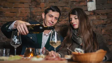 Mann schenkt Wein in Gläser, während Frau zusieht.