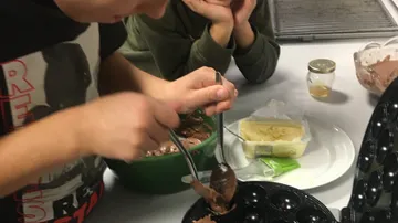 Boy scoops chocolate mix into a waffle machine; kitchen.